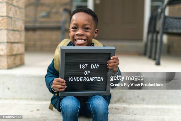 a cute boy holding up a first day of kindergarten sign - holding sign stock pictures, royalty-free photos & images