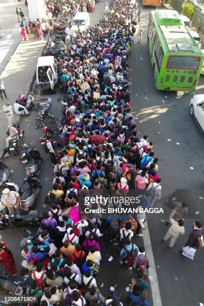 Migrant workers and their family members lineup outsdie the Anand Vihar bus terminal to leave for their villages during a government-imposed...