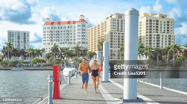beautiful adventurous couple run down a dock in swimwear holding hands - west palm beach stock pictures, royalty-free photos & images