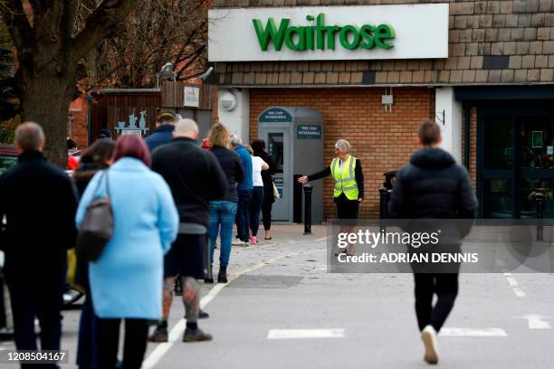 Member of staff enforces social distancing rules in a queue outside a Waitrose supermarket in Frimley, south west of London on March 29 as life in...