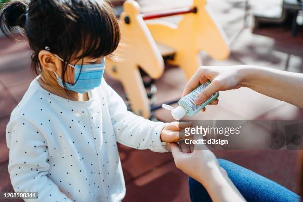 young mother squeezing hand sanitizer onto little daughter's hand in the playground to prevent the spread of viruses - infection prevention stockfoto's en -beelden