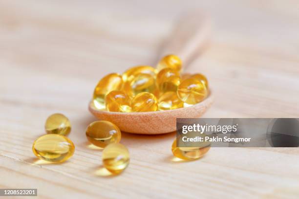 fish oil capsules with omega 3 and vitamin d on spoon wood with wooden background, healthy diet concept. - vitamine d stockfoto's en -beelden