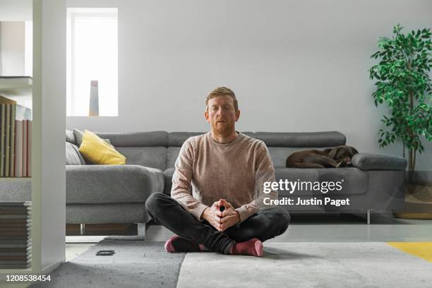 man practising meditation in living room - man meditating stock pictures, royalty-free photos & images