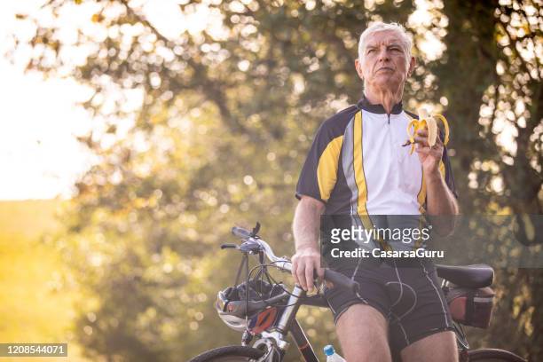 actieve hogere volwassen fietser die rust en een banaan eet - sportsperson stockfoto's en -beelden