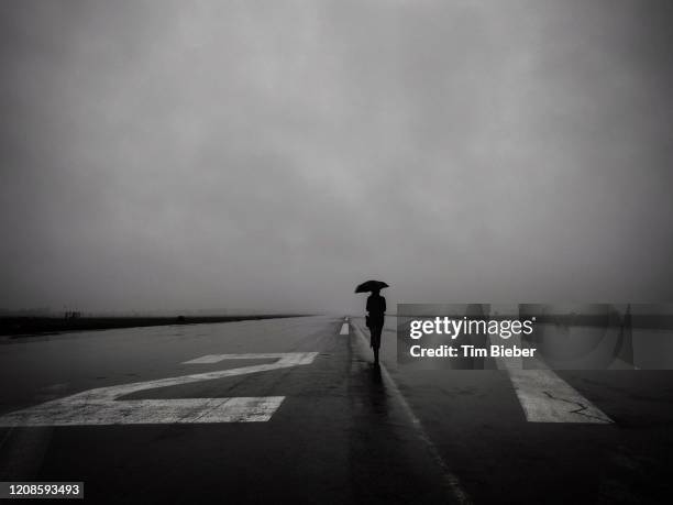 lone woman with umbrella on empty runway 27 left at tempelhof airport in berlin on a rainy day. - berlin airlift 個照片及圖片檔