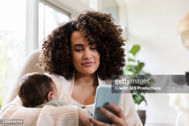 nueva mamá usa smarphone en casa - mom holding baby fotografías e imágenes de stock