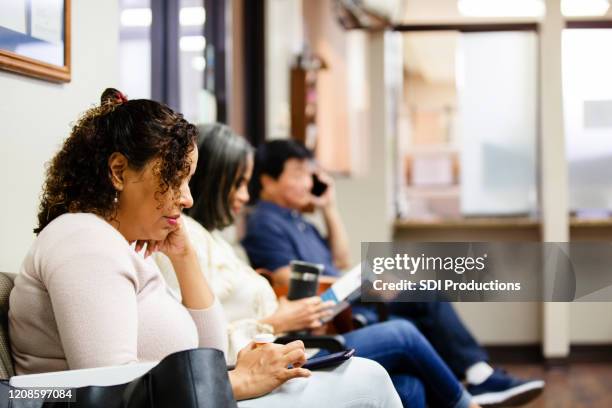 mensen kijken naar brochure en gebruiken smartphones tijdens het wachten - wachtkamer stockfoto's en -beelden