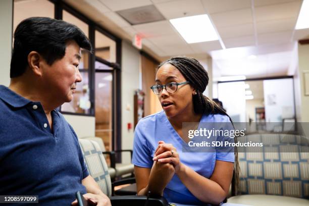 mid adult nurse explains procedure to man in waiting room - visit us stock pictures, royalty-free photos & images