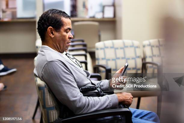 mature adult man uses smart phone while waiting - doctor smartphone stock pictures, royalty-free photos & images