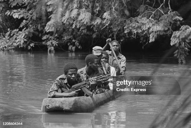 Guinean rebel soldiers, the lead soldier armed with an AK47 assault rifle, as they patrol a river in a pirogue during the Guinea-Bissau War of...