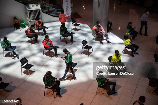 Motorbike food delivery drivers wait to pick up orders in organized "social distancing" chairs in Central Plaza Pinklao Mall on March 30, 2020 in...