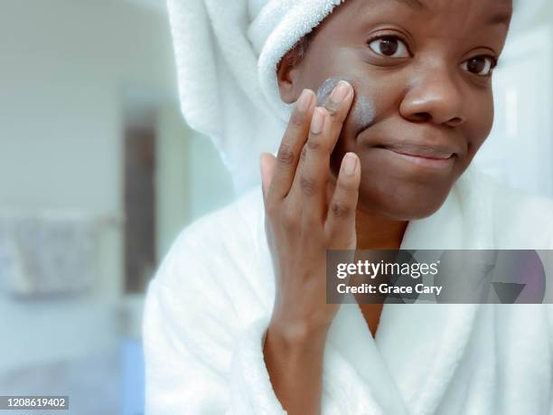 woman smooths moisturizer onto face after morning shower - brightly lit bathroom stock pictures, royalty-free photos & images