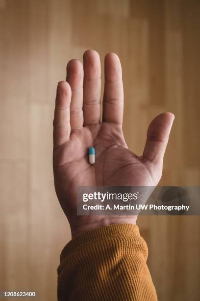 a man's hand holding a pill with a wood floor as background - finger tablet stock pictures, royalty-free photos & images