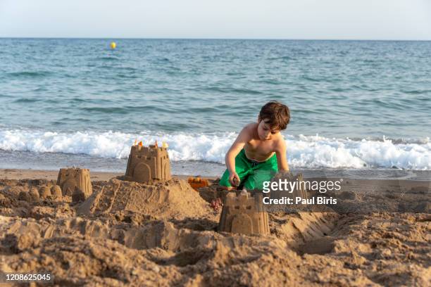 boy making castles in the sand of the shore of the beach, costa blanca, spain - château de sable photos et images de collection