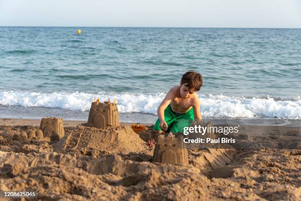 boy making castles in the sand of the shore of the beach, costa blanca, spain - benidorm stock pictures, royalty-free photos & images