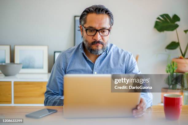 homem usando laptop em casa - handsome mexican men - fotografias e filmes do acervo