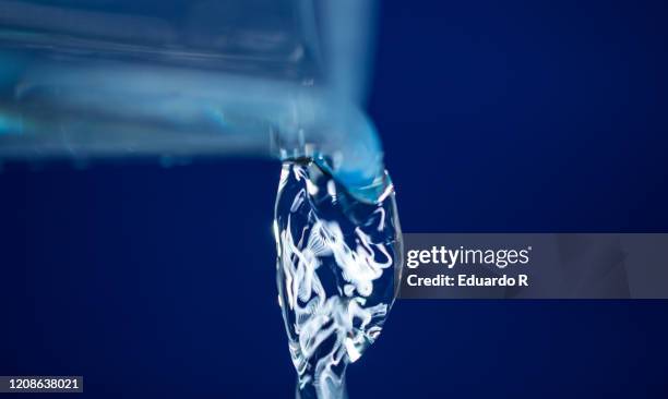 glass pouring water close up with blue background - water bottle splash stock pictures, royalty-free photos & images