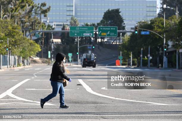 Woman wears a mask as she crosses an empty street near the Los Angeles Convention Center in downtown Los Angeles California March 30, 2020. - The...