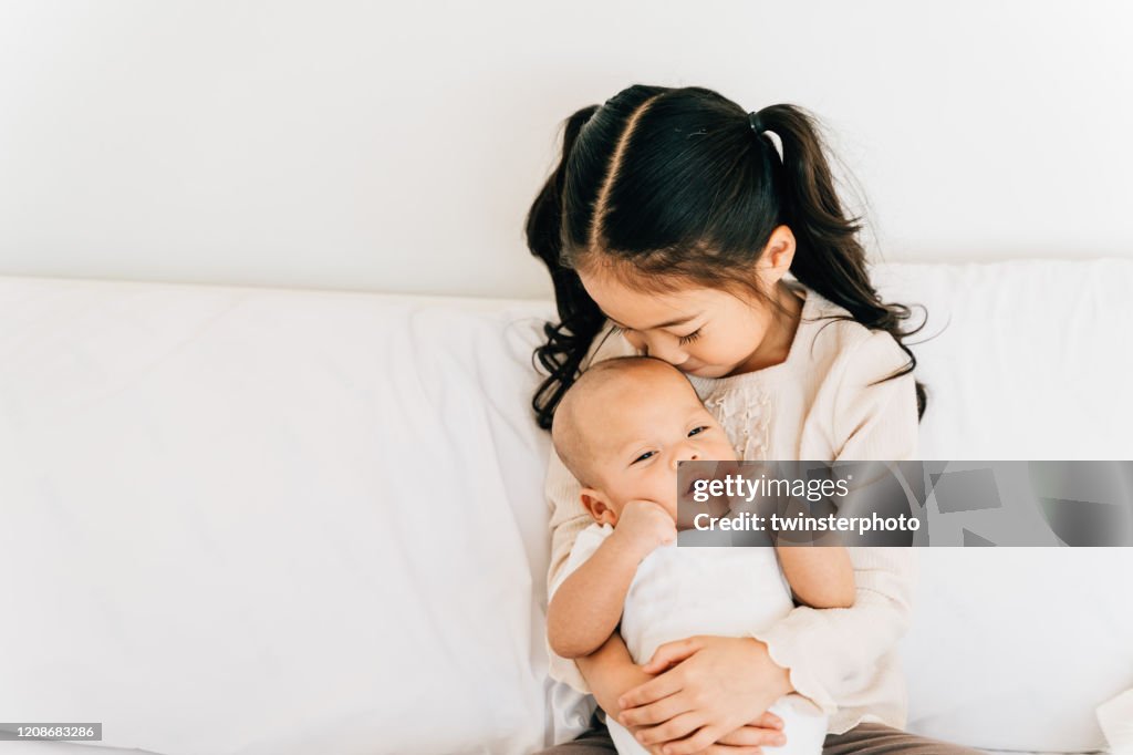 Asian child hugging newborn baby on bed