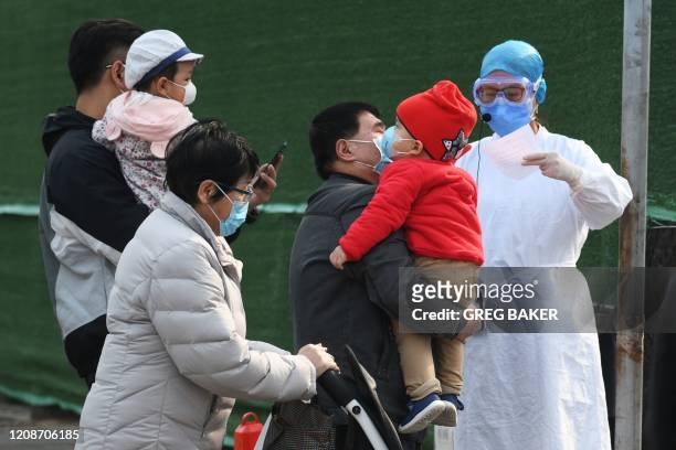 Families wait to enter a children's hospital near hospital staff wearing protective gear as a precautionary measure against the COVID-19 coronavirus...