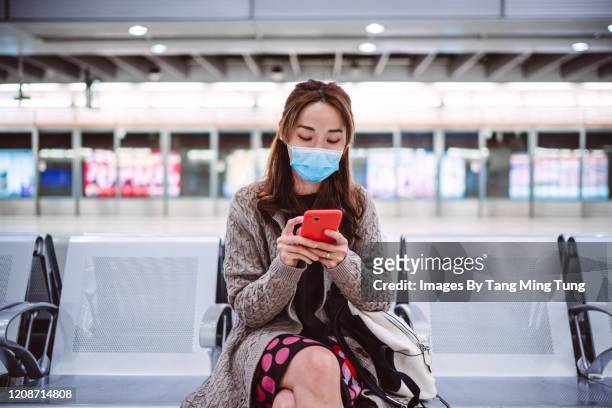 young asian lady in medical face mask using smartphone joyfully on train platform - subway bench bildbanksfoton och bilder
