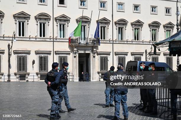 Police officers stand by as the Italian flag and the flag of Europe fly at half-mast on Palazzo Chigi government building in Rome on March 31, 2020...