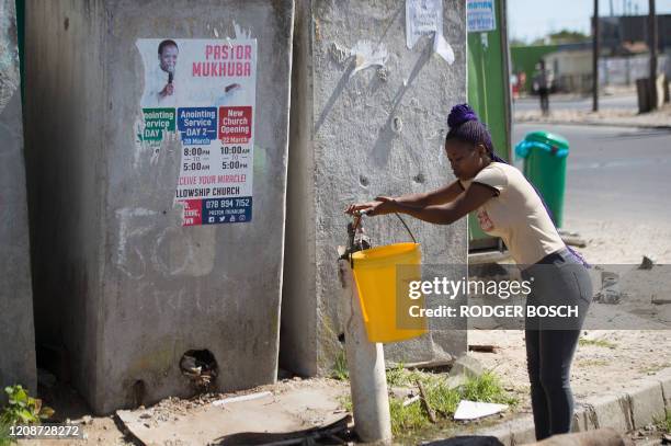Woman fills a bucket from a communal tap in front of a line of communal toilets in Khayelitsha, near Cape Town, on March 31, 2020. - Local government...
