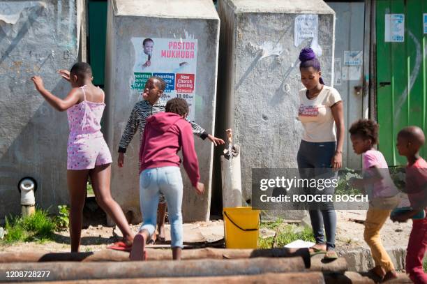 Woman fills a bucket from a communal tap as children play in front of a line of communal toilets in Khayelitsha, near Cape Town, on March 31, 2020 in...