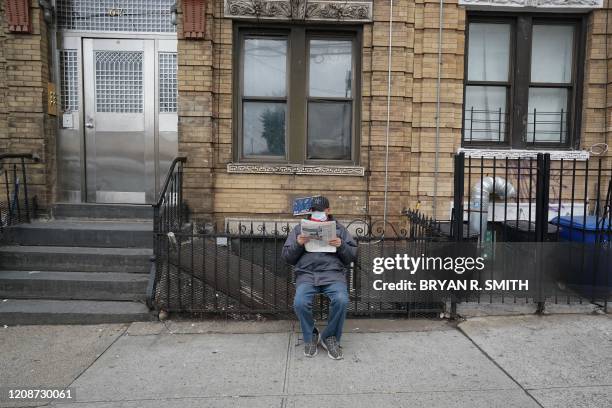 Man wearing a surgical mask reads the newspaper on the sidewalk in the Bushwick section of the Borough of Brooklyn on March 31, 2020 in New York. - A...