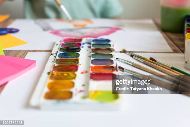 The child paints. Watercolor, gouache, paint brushes, colored and wax crayons, stickers. Set for drawing, creativity, hobbies