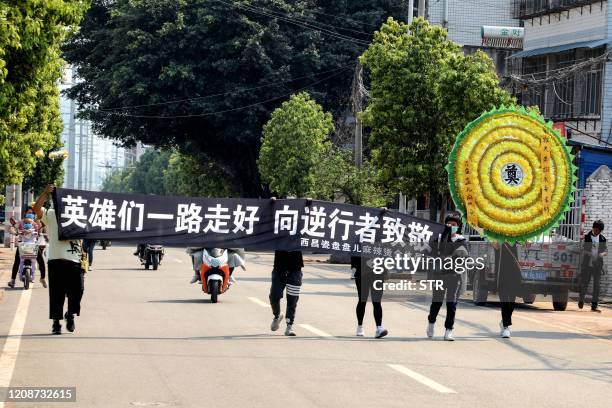 This photo taken on March 31, 2020 shows people carrying a banner showing respect to firefighters and the forestry guide who were killed while...