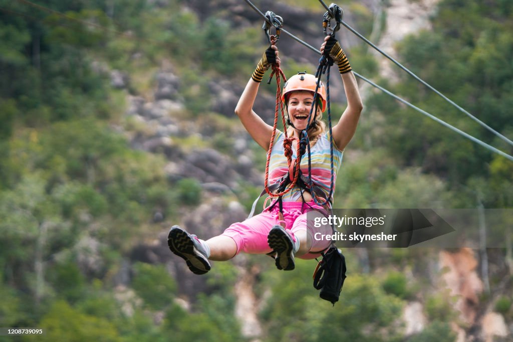 Mujer alegre divirtiéndose durante el recorrido en canopy en el bosque.