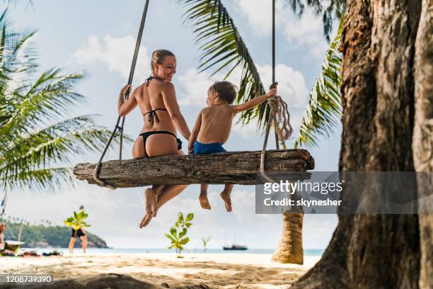 vue arrière d’une mère célibataire heureuse et fils balançant sur la plage. - balançoire photos et images de collection