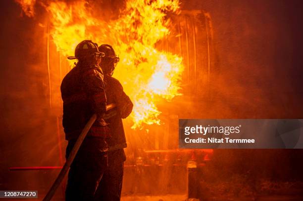 side view of firefighter in fire fighting operation using extinguisher and water from hose for fire fighting. - australia fire - fotografias e filmes do acervo