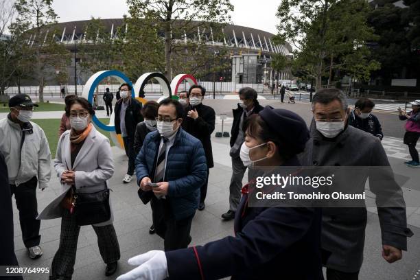 People wearing face masks walk past the Olympic rings in front of the new National Stadium, the main stadium for the upcoming Tokyo 2020 Olympic and...