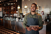 Cheerful young male owner holding digital tablet while standing in cafe