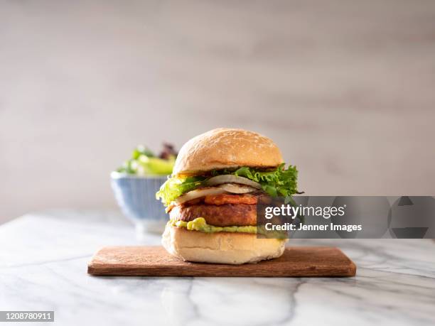 vegan burger on a chopping board. bowl of salad in the background. - vegetarianism - fotografias e filmes do acervo