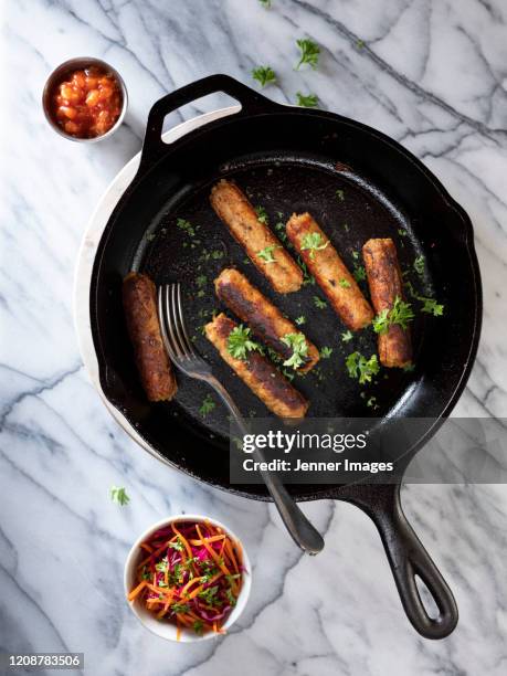 vegan sausages in a frying pan on a white marble table. - vegan sausage stock pictures, royalty-free photos & images