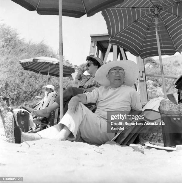 Italian director Mario Camerini relaxing under a beach umbrella on the set of the film Ulysses. 1953