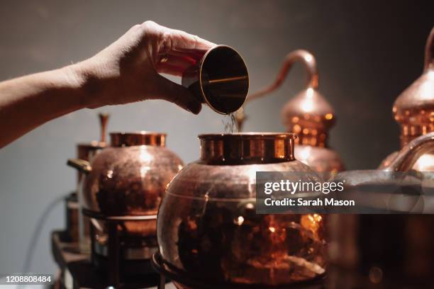 hand pouring liquid into copper still - distilleria foto e immagini stock