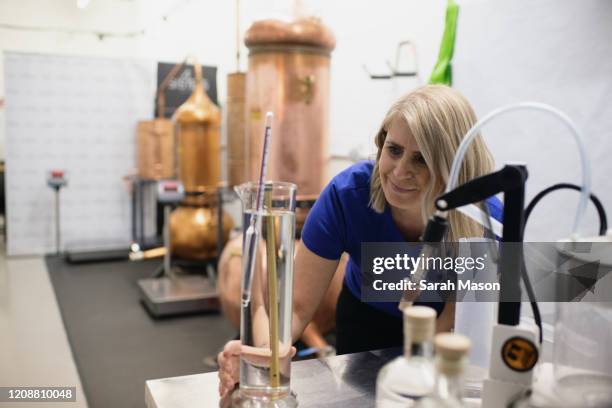 woman in distillery checking liquid in glass container - distilleria foto e immagini stock