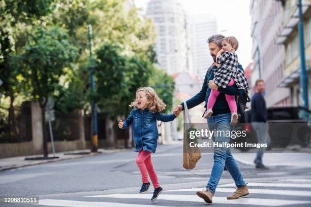 father with small girls walking outdoors in city, crossing the road. - young white people walking stock-fotos und bilder