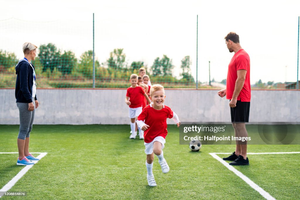 A group of children with coach training on football pitch.