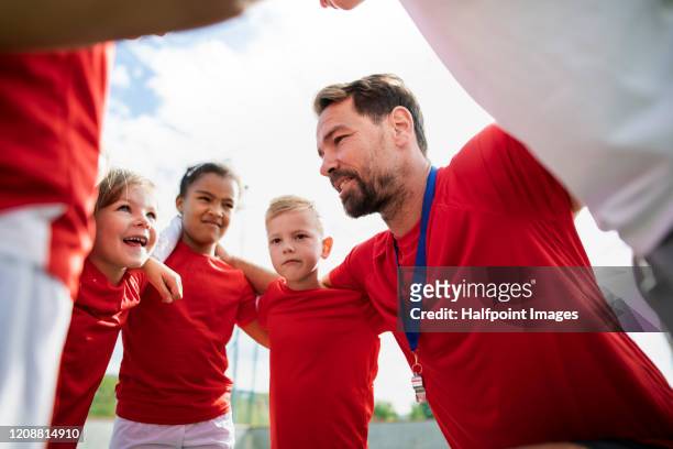a group of children with coach standing in circle outdoors on football pitch. - coach stock pictures, royalty-free photos & images