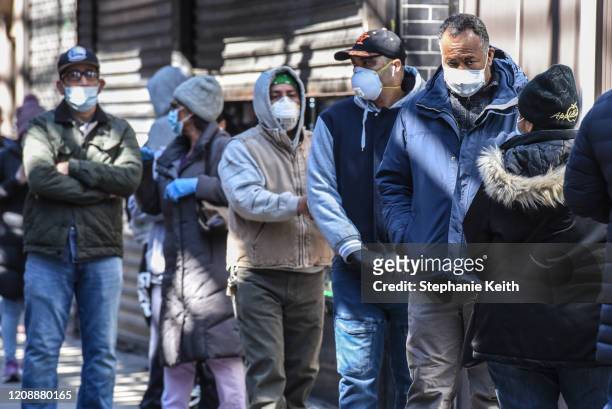 People stand in line while wearing face masks in the Elmhurst neighborhood on April 1, 2020 in New York City. With more than 75,000 confirmed cases...