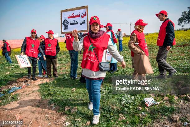 Man wearing a vest and hat showing the Moroccan national flag and with the Arabic slogan "long live the King, down with the real estate mafia", holds...