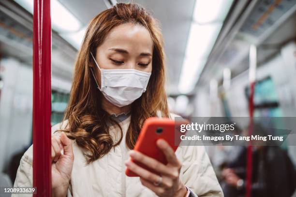 young asian lady in medical face mask using smartphone in train - u bahnzug stock-fotos und bilder