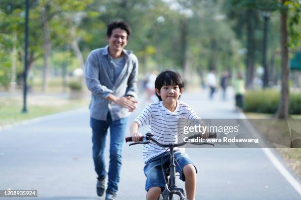 father teach son to ride a bicycle at park - boy thailand stock pictures, royalty-free photos & images