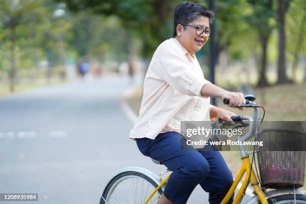 senior woman riding exercise relaxing bicycle at park - fat asian woman stock-fotos und bilder