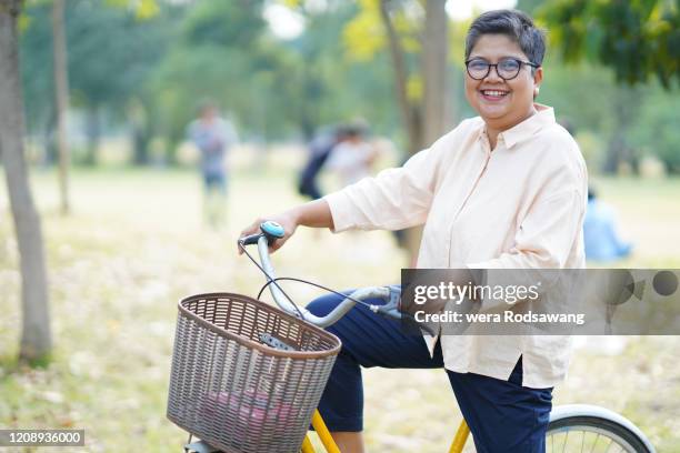 senior woman riding bike relaxing at park - fat asian woman stock-fotos und bilder